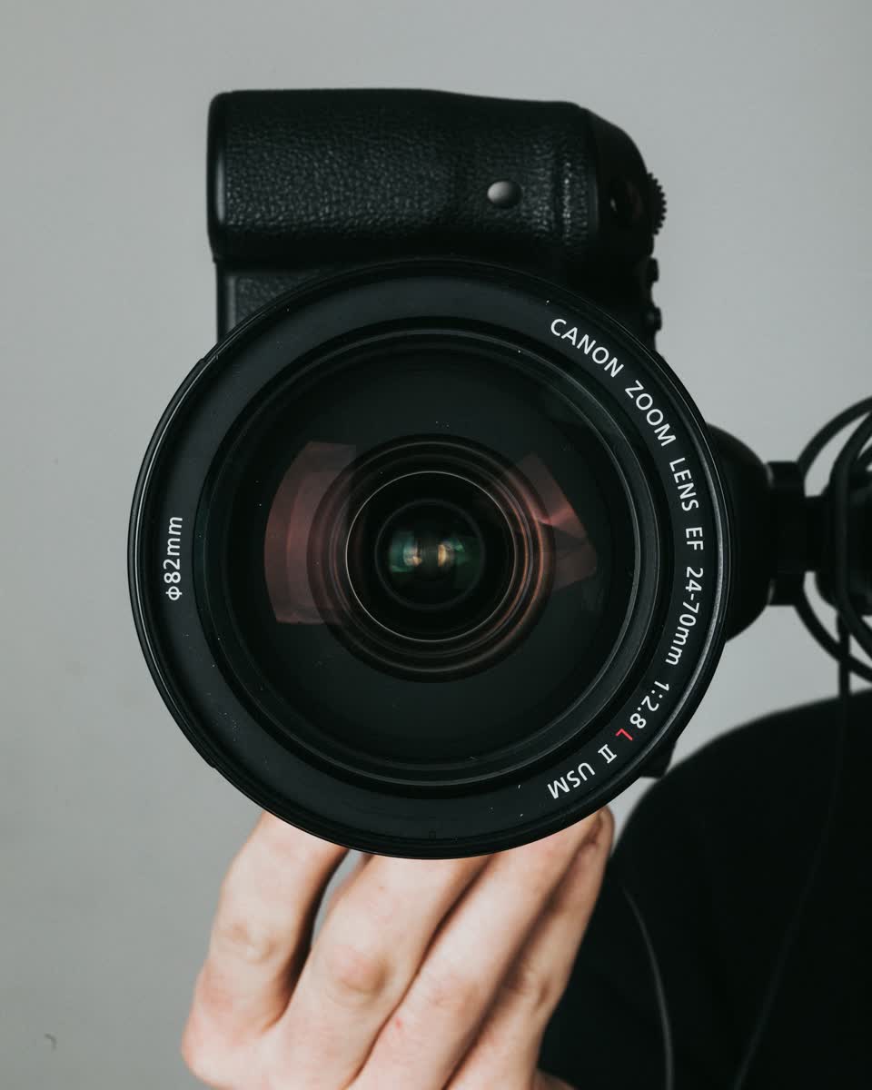 Hand hält eine Kamera mit großem Zoomobjektiv