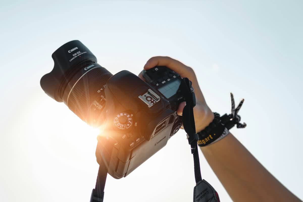 Hand hält eine Spiegelreflexkamera gegen hellen Himmel