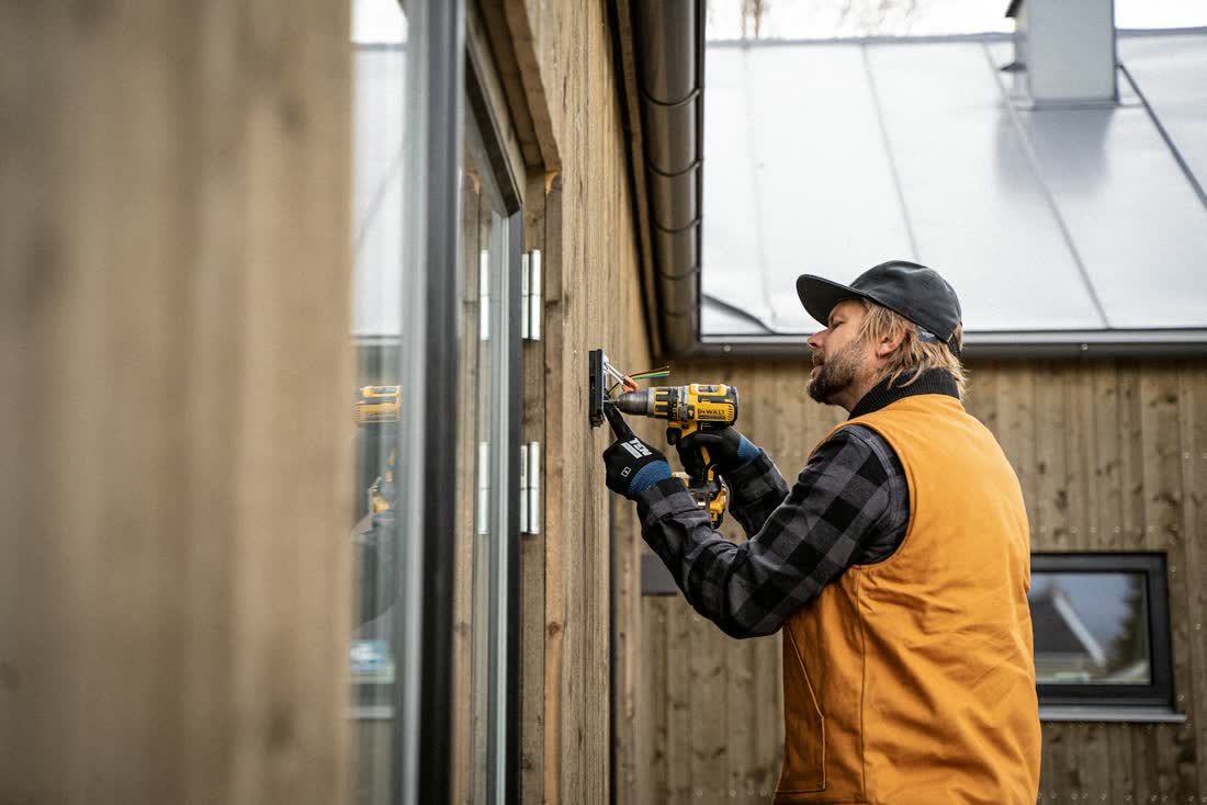Handwerker setzt mit dem Akkuschrauber ein Fenster in eine Holzfassade.